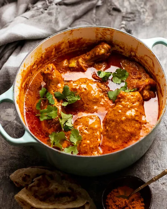 Butter chicken masala in a pot with naan and coriander